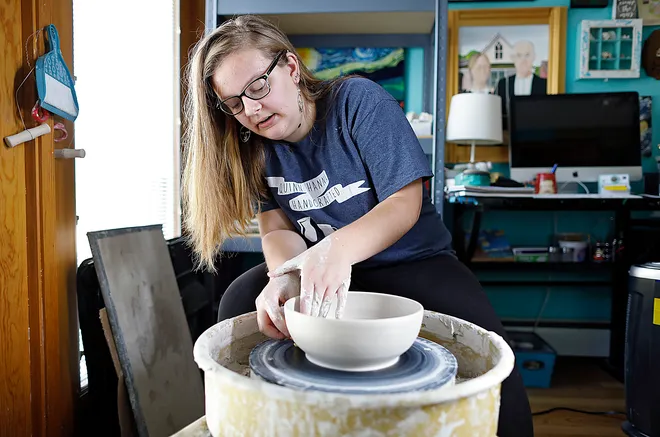 Bespectacled student throuwing a pot on a wheel.